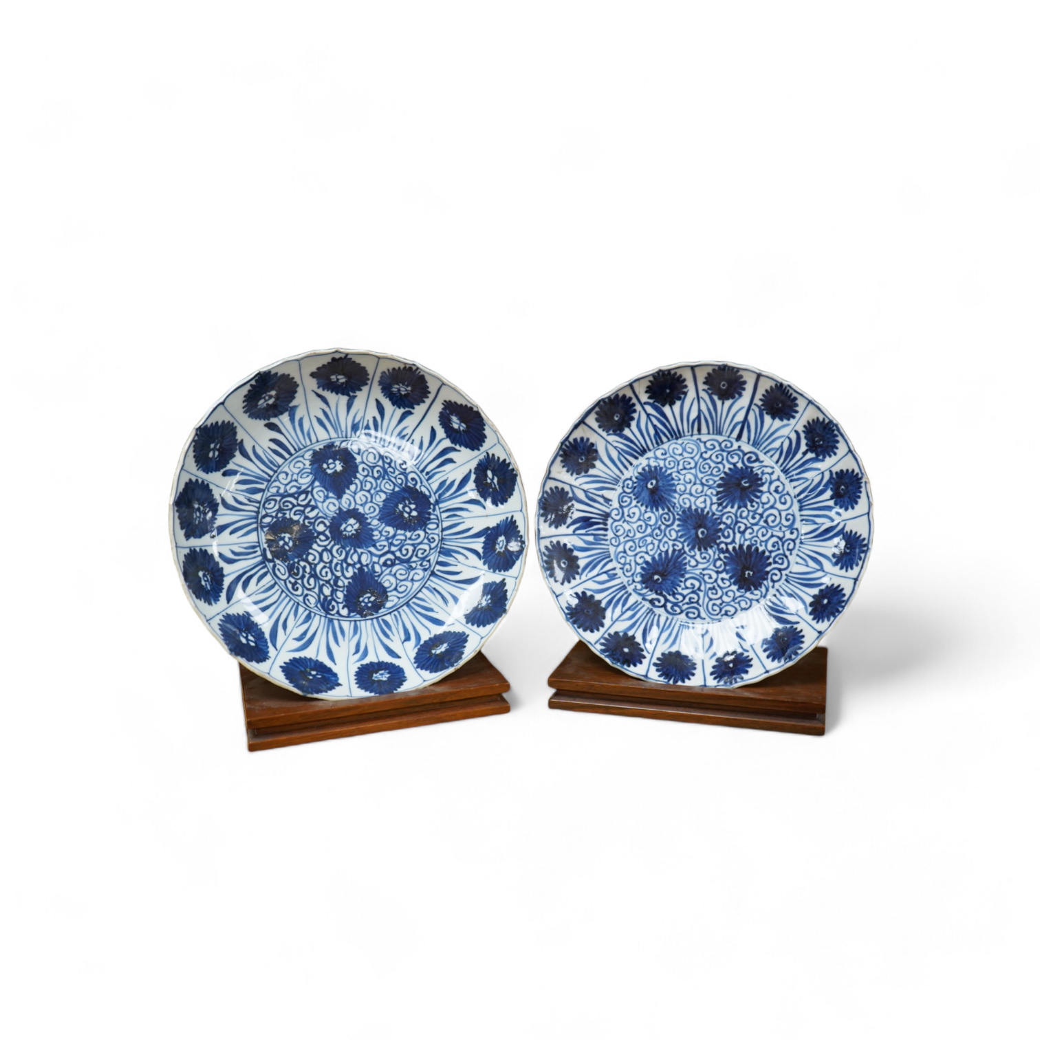 Two Chinese blue and white ‘astor’ plates, Kangxi period, with hardwood stands, largest 22cm diameter. Condition - poor to fair